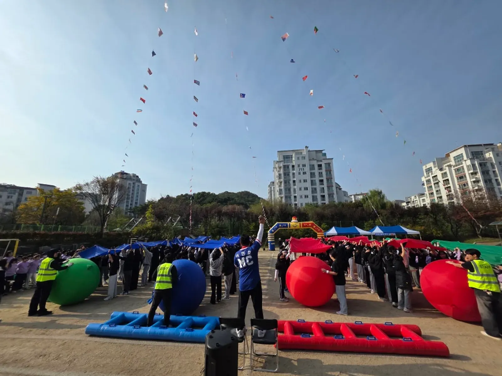 운동장에 에어 사다리와 대형 공을 놓고 양쪽 팀이 겨루는 경기장과 안전조끼 입은 요원들