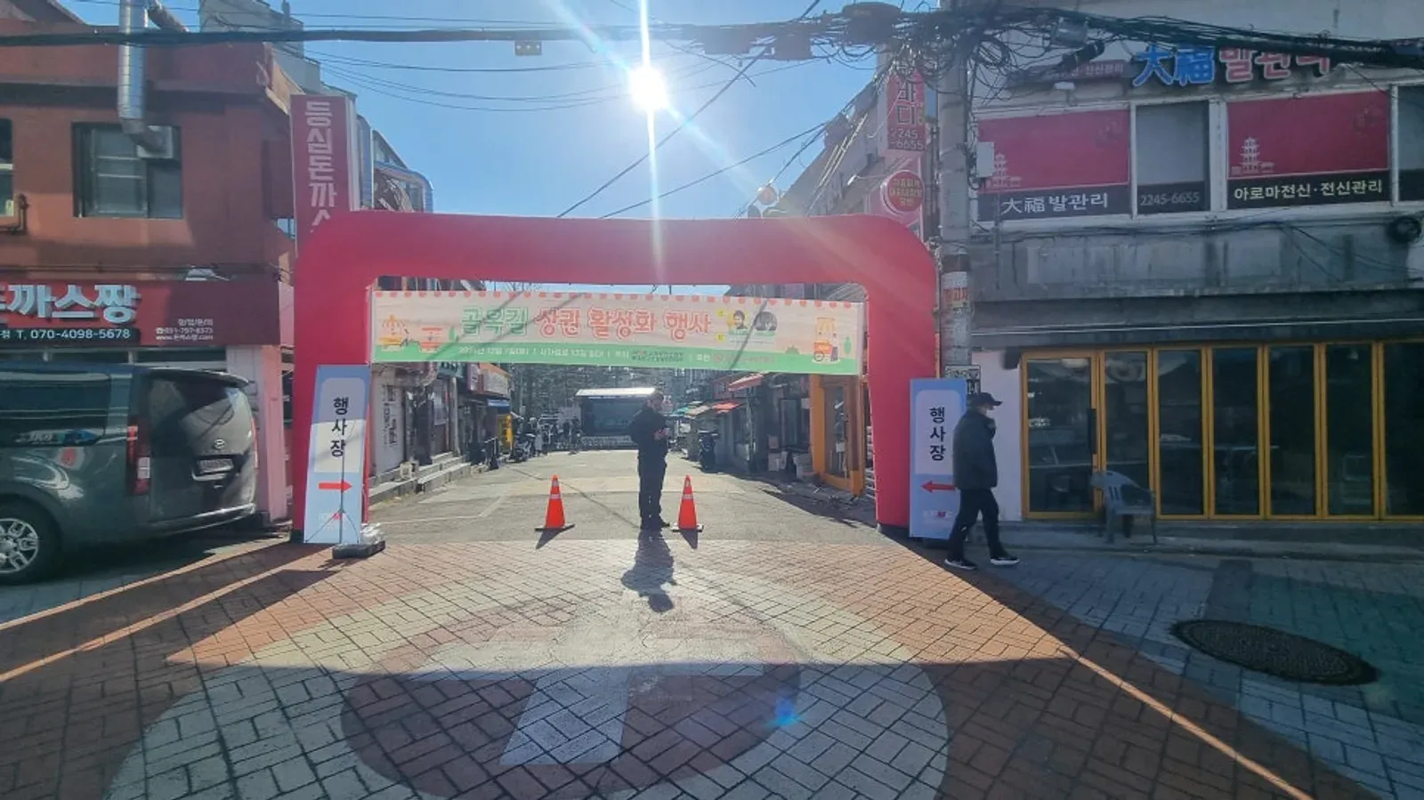 골목 입구에 빨간 아치와 라바콘을 세워 차량을 막고 축제장 입구를 만든 모습